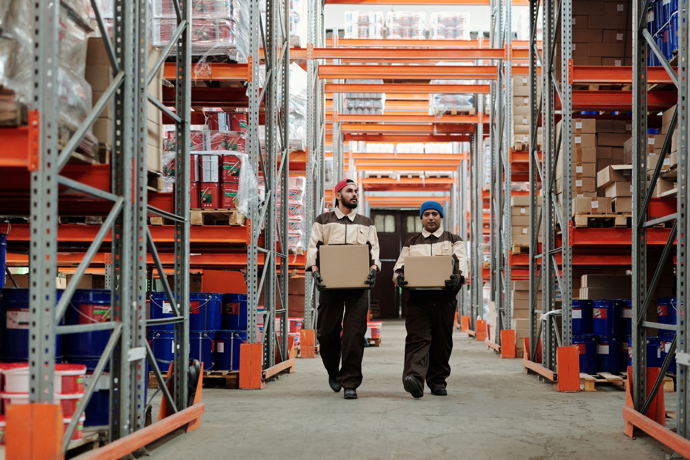 Warehouse workers carrying cardboard boxes between storage racks